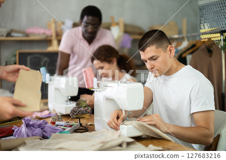Young man stitching at machine during sewing class for adults 127683216
