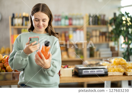 European teen girl customer at shop scans QR code on grapefruit juice bottle using phone camera 127683230
