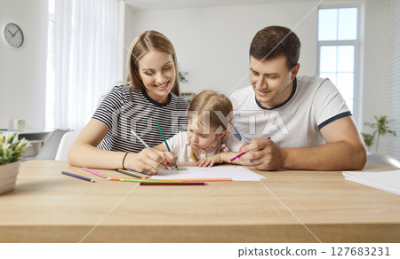 Parents sitting at table with daughter and drawing in the living room at home Parents sitting at table with daughter and drawing in the living room at home 127683231