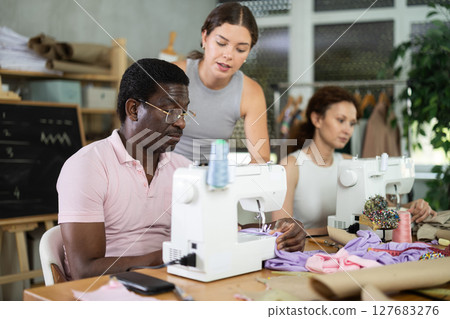 Students work with sewing machines under guidance of teacher Students work with sewing machines under guidance of teacher 127683276