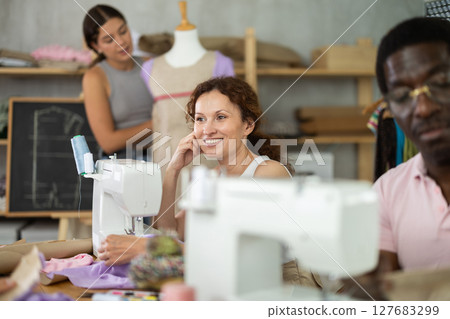 Smiling woman stitching fabric on machine in sewing class for adults 127683299