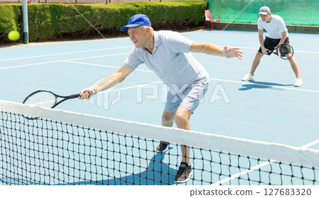 Elderly male player serving ball during training tennis in court outdoors 127683320