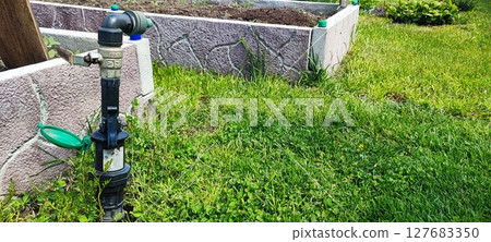 Eco-friendly garden irrigation setup with hose valve and drip system for sustainable backyard watering near raised beds Eco-friendly garden irrigation setup with hose valve and drip system for sustainable backyard watering near raised beds 127683350