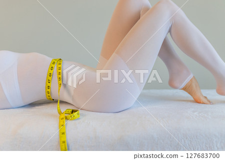 woman in a white suit for LPG massage holds a centimeter in her hands. Anti-cellulite body care concept. Gray background 127683700