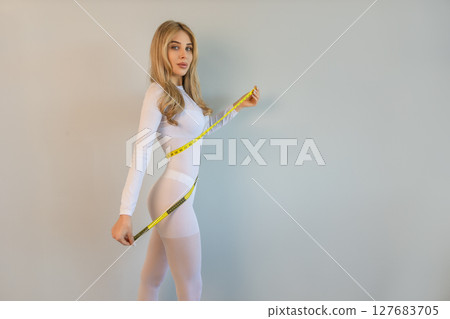woman in a white suit for LPG massage holds a centimeter in her hands. Anti-cellulite body care concept. Gray background 127683705