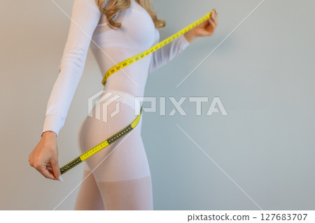 woman in a white suit for LPG massage holds a centimeter in her hands. Anti-cellulite body care concept. Gray background 127683707