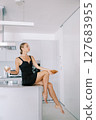Young woman with a croissant and coffee in her hands sits on a table in the kitchen and looks away 127683955
