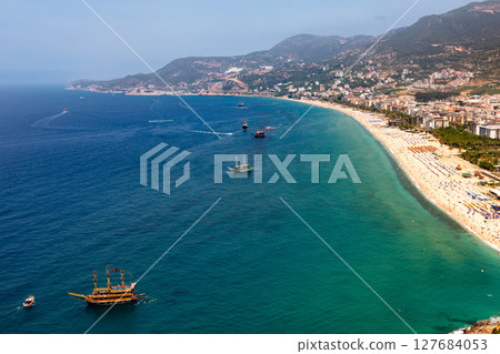 Panoramic aerial view of Alanya coastline with tourist boats and crowded sandy beach along the Mediterranean Sea 127684053