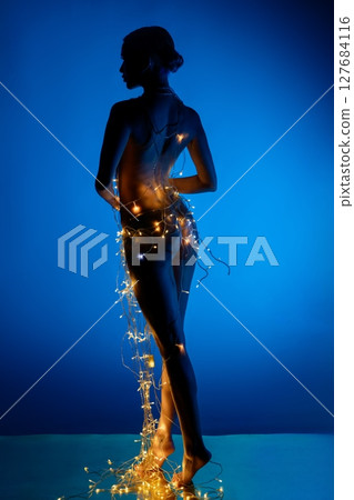 Silhouette of a woman adorned with lights in a serene blue atmosphere Silhouette of a woman adorned with lights in a serene blue atmosphere 127684116