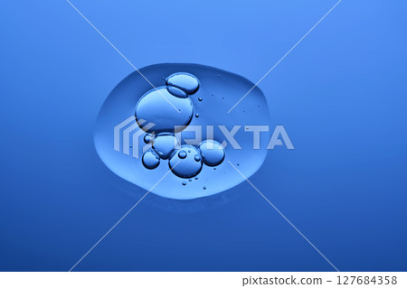 A drop of serum or other cosmetic product on a dark blue background. 127684358