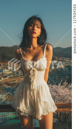 Beautiful Korean woman posing in a white dress against a scenic mountain backdrop during sunset Beautiful Korean woman posing in a white dress against a scenic mountain backdrop during sunset 127684568