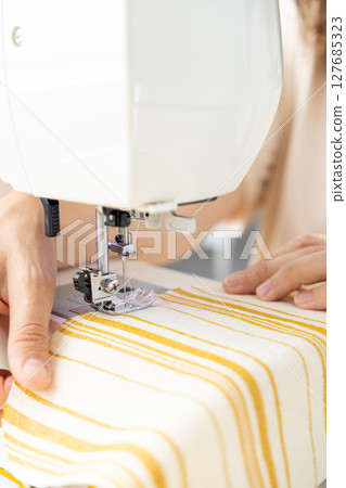 woman sews a light fabric on a sewing machine. making clothes, hobbies. 127685323