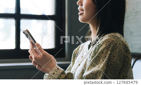 Young woman sitting on the couch and using a smartphone Young woman sitting on the couch and using a smartphone 127685479