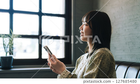 Young woman sitting on the couch and using a smartphone Young woman sitting on the couch and using a smartphone 127685480