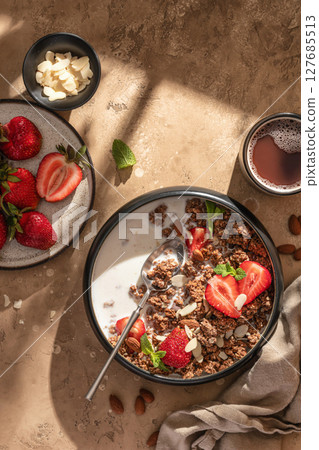 Healthy breakfast: fresh granola, muesli with milk, strawberry and almond for breakfast on brown textured background in bright morning light. Vertical Healthy breakfast: fresh granola, muesli with milk, strawberry and almond for breakfast on brown textured background in bright morning light. Vertical 127685513