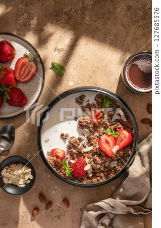 Healthy breakfast: fresh granola, muesli with milk, strawberry and almond for breakfast on brown textured background in bright morning light. Top view Healthy breakfast: fresh granola, muesli with milk, strawberry and almond for breakfast on brown textured background in bright morning light. Top view 127685576
