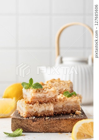 Lemon crumble bars on wooden cutting board on white tile background with text space. Oatmeal lemon bars 127685606