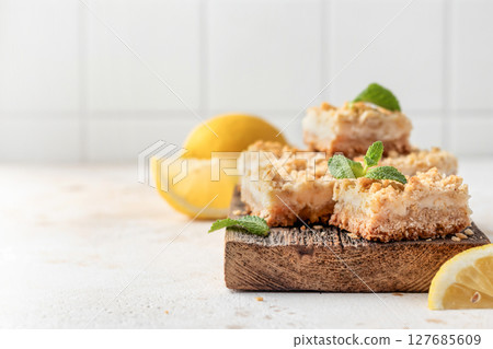 Lemon crumble bars on wooden cutting board on white tile background with text space. Oatmeal lemon bars 127685609
