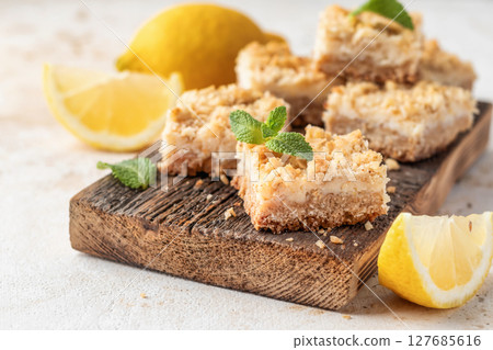 Lemon crumble bars on wooden cutting board on white textured background. Oatmeal lemon bars Lemon crumble bars on wooden cutting board on white textured background. Oatmeal lemon bars 127685616