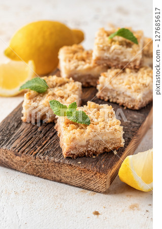 Lemon crumble bars on wooden cutting board on white textured background, oatmeal lemon bars 127685617