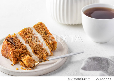 Homemade layered carrot cake with cream cheese, walnuts and spices on a plate with tea Homemade layered carrot cake with cream cheese, walnuts and spices on a plate with tea 127685633