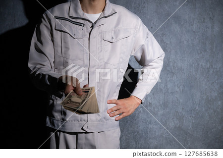 A man wearing work clothes is holding a stack of bills A man wearing work clothes is holding a stack of bills 127685638