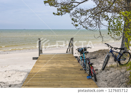 Boardwalk to Baltic Sea beach with bicycles resting under tree 127685712