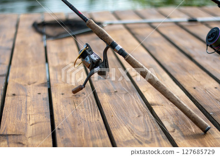 Spinning and reel on the background of wooden pier. Professional tackle for catching predatory fish. 127685729