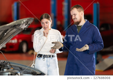 Mechanic checking young woman client car in car service center 127686008