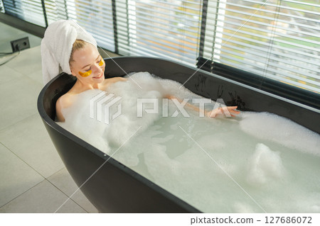 Spa relaxation. Young woman lying in bath with foam bubbles. Girl relaxing in bathroom at home. Pretty female spending morning in bathroom enjoying taking bath. Beauty treatment body skin care concept 127686072