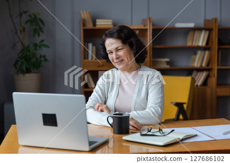 Happy middle aged senior woman sit with laptop talk on video call with friends family. Laughing mature old senior grandmother having fun talking speaking with grown up children online 127686102