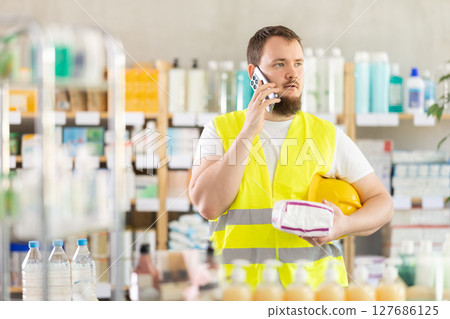 Male builder in a yellow vest consults on his mobile phone when buying feminine pads Male builder in a yellow vest consults on his mobile phone when buying feminine pads 127686125