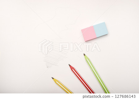 Three colored pencils and an eraser on white paper. 127686143