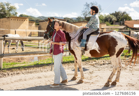 Happy mother leads horse with his son on it - walk around horse farm 127686156