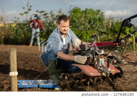Man repairing cultivator with tools 127686180
