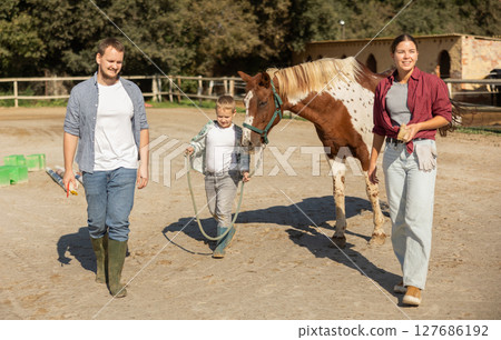Father, mother and son riding horse together at small horse farm Father, mother and son riding horse together at small horse farm 127686192