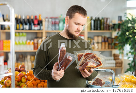 Male shopper chooses between dried sausages and jamon in grocery supermarket Male shopper chooses between dried sausages and jamon in grocery supermarket 127686198