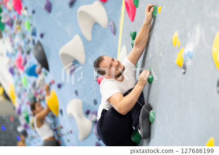 Man climbing a tall, indoor, man made rock climbing wall Man climbing a tall, indoor, man made rock climbing wall 127686199