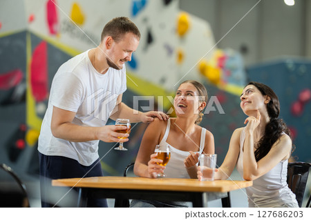 Man and two girls meet after rock climbing training - discussing successes and failures together at table, chatting and drinking beer 127686203