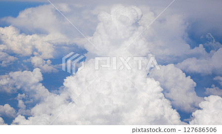 Large snow-white cumulus clouds against the background of a blue sky, view from the window of an airplane. Large snow-white cumulus clouds against the background of a blue sky, view from the window of an airplane. 127686506