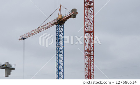 There are two construction cranes in the sky, one red and blue, and the other white. 127686514