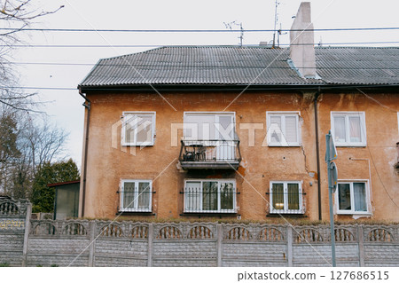 old brown building with a balcony. The building is surrounded by a fence.  127686515