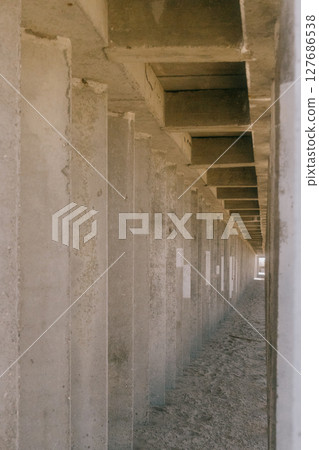 Long, narrow hallway with concrete pillars. The pillars are grey and the hallway is empty. 127686538
