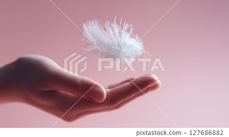 Hand Holding Feathery Light Element on Soft Pastel Background 127686882