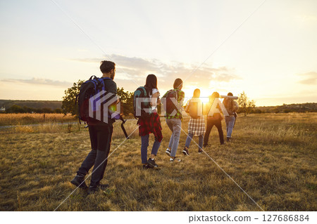Group male and female Caucasian tourists walk in row one after other on flat green lawn. 127686884