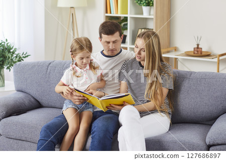 Happy loving family at home, young father, mother holding reading book, parents with cute child Happy loving family at home, young father, mother holding reading book, parents with cute child 127686897