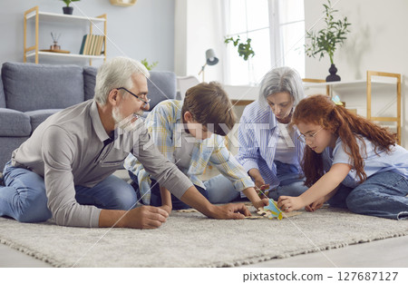 Grandmother, grandfather and grandchildren playing on the floor in a puzzle at home 127687127