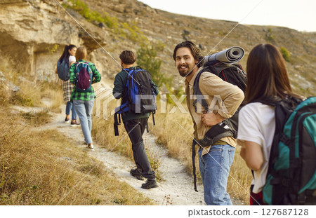 Portrait of smiling male hiker with backpack walking to top of mountain with his fellow hikers. Portrait of smiling male hiker with backpack walking to top of mountain with his fellow hikers. 127687128