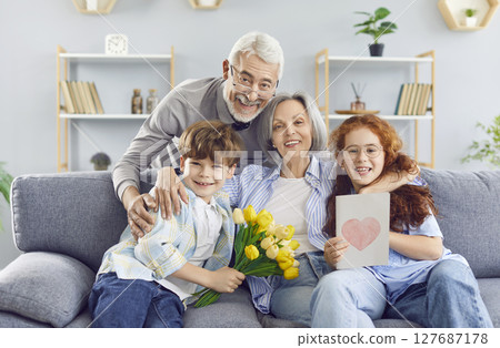 Senior grandparents sitting on sofa at home with grandchildren. Celebration and holiday concept. Senior grandparents sitting on sofa at home with grandchildren. Celebration and holiday concept. 127687178