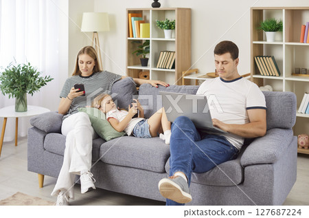 Young family at home enjoy using laptop and smartphones sitting on sofa, entertaining online  127687224